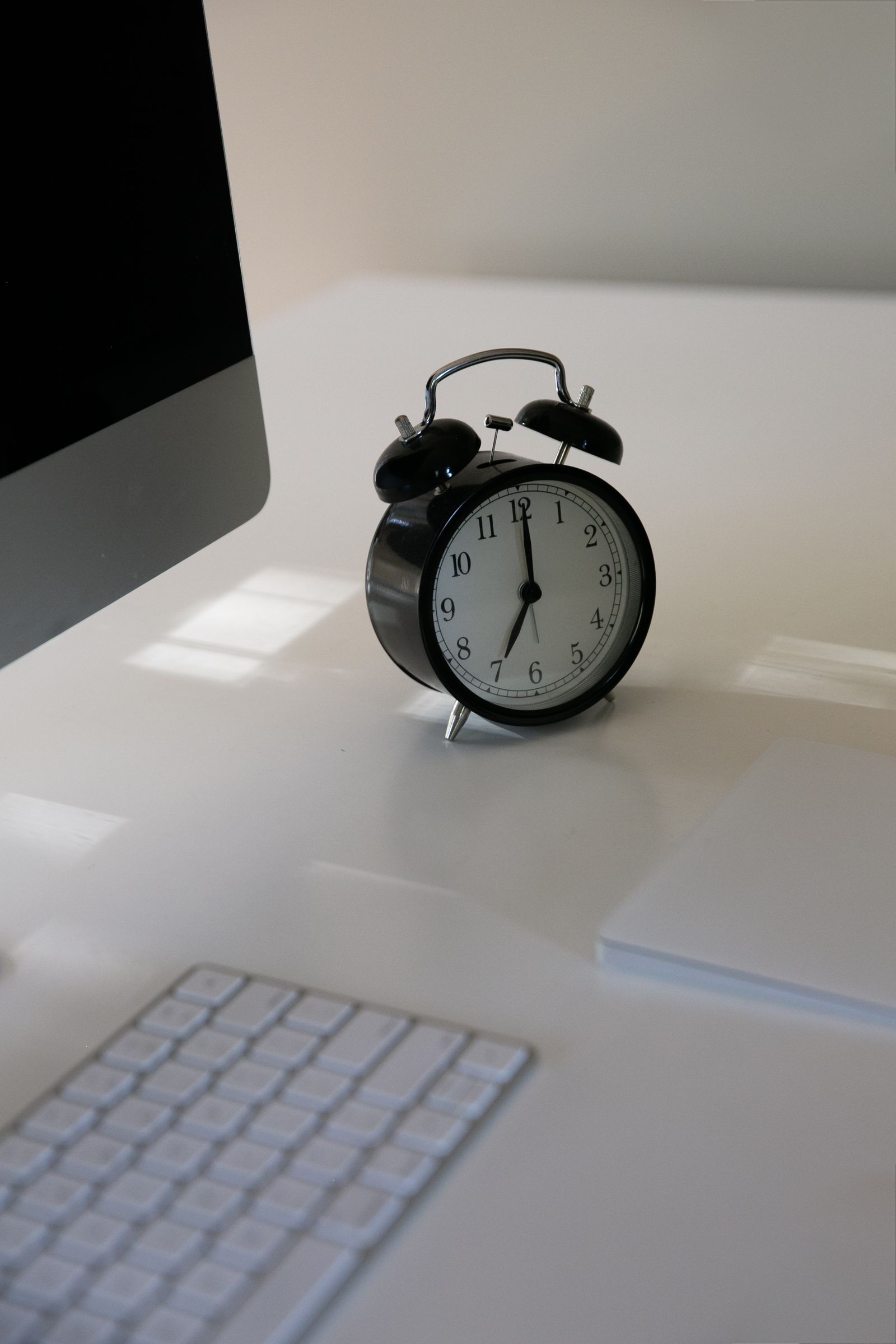 Despertador vintage preto ao lado de um computador e teclado em mesa de escritório