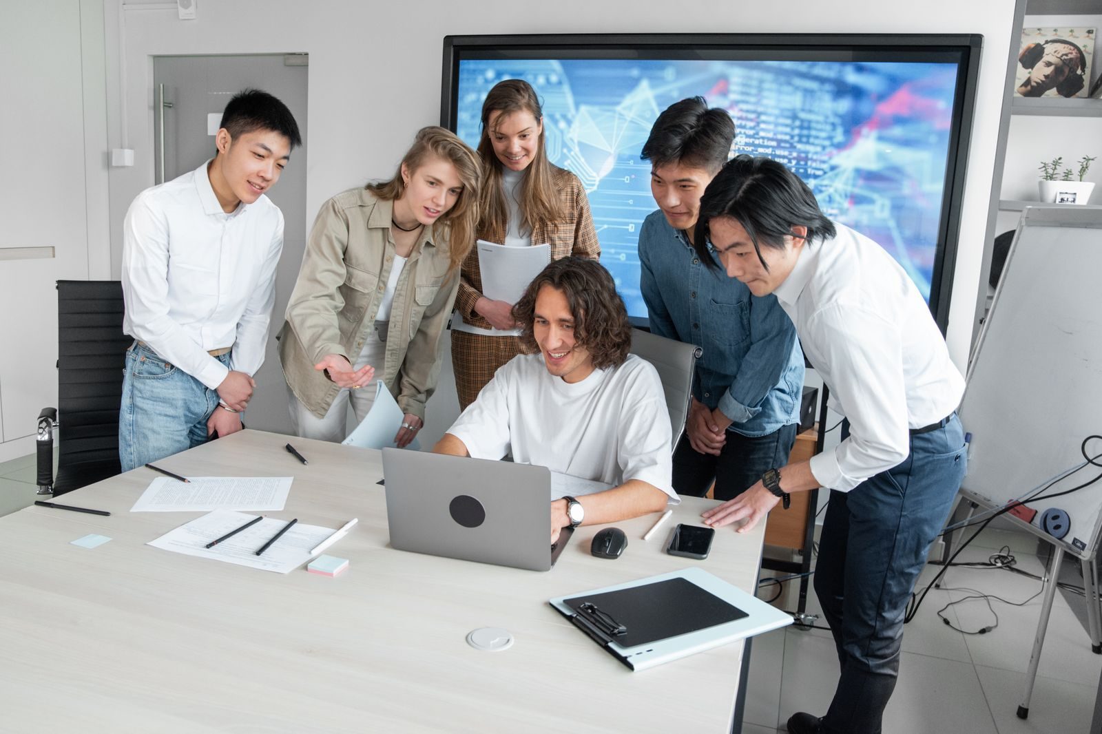 Profissional explica algo no notebook para colegas reunidos em volta da mesa do escritório