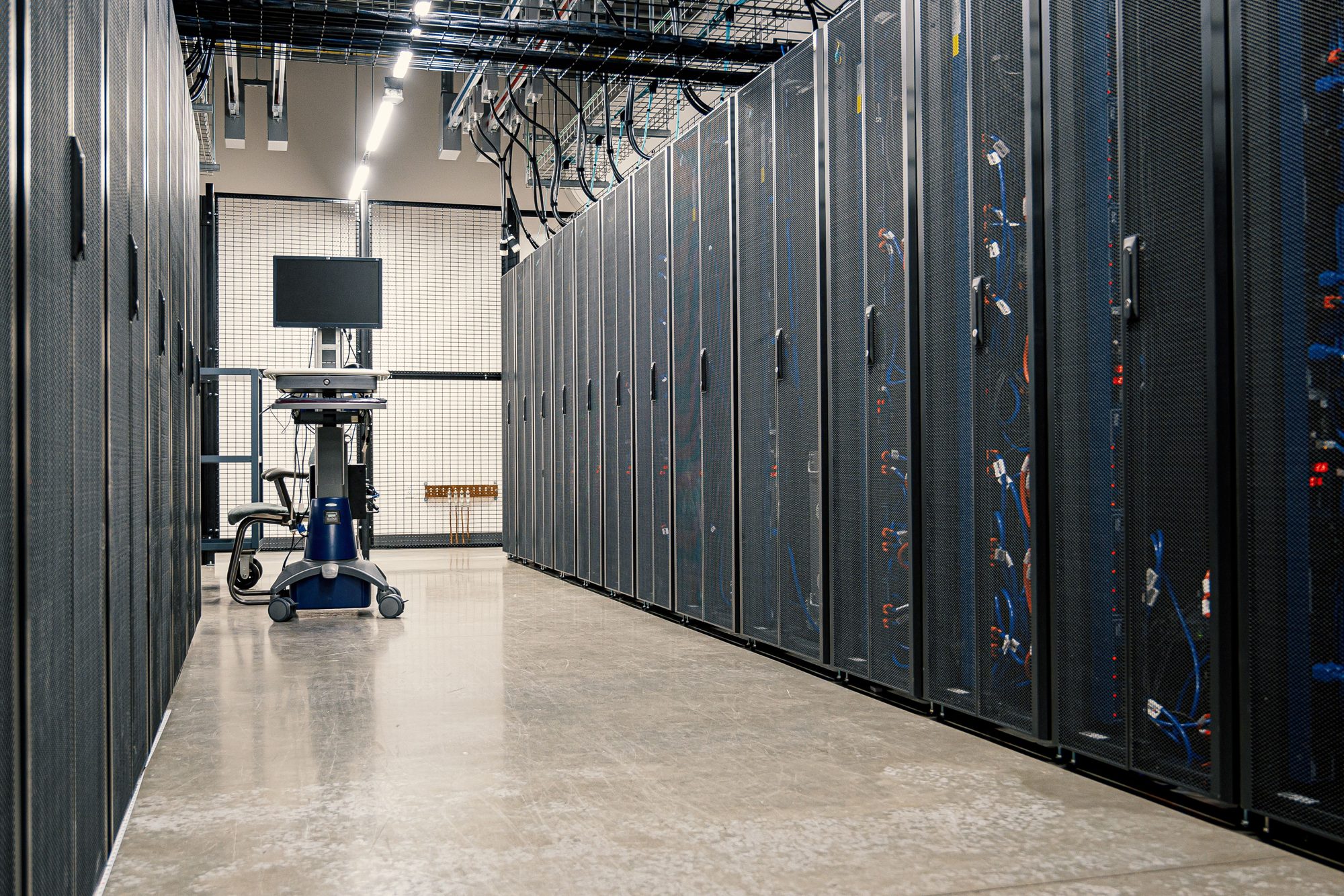 Corredor de data center com racks de servidores, simbolizando a infraestrutura de dados por trás da IA
